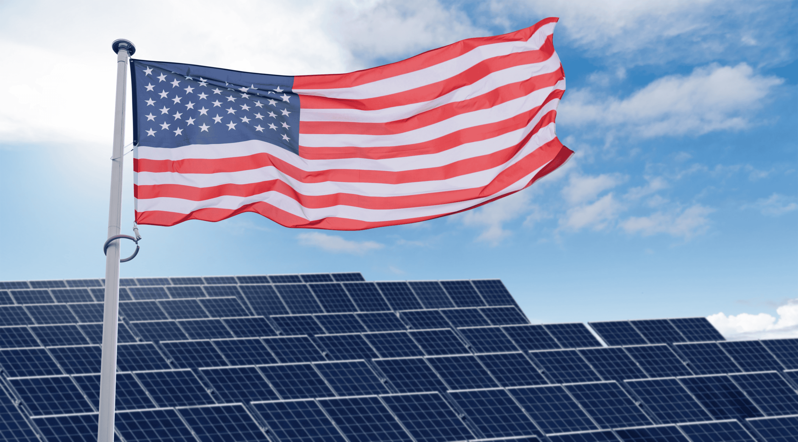 An American flag waves above solar panels under a blue sky.