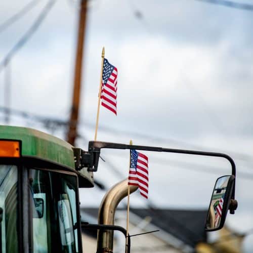 A vehicle with two small American flags near the mirror against a cloudy sky background.